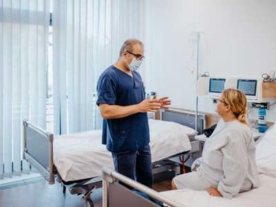 Plastischer Chirurg erklärt einer Patientin auf der Station den Ablauf einer Lipödem-OP – vertrauensvolle medizinische Beratung